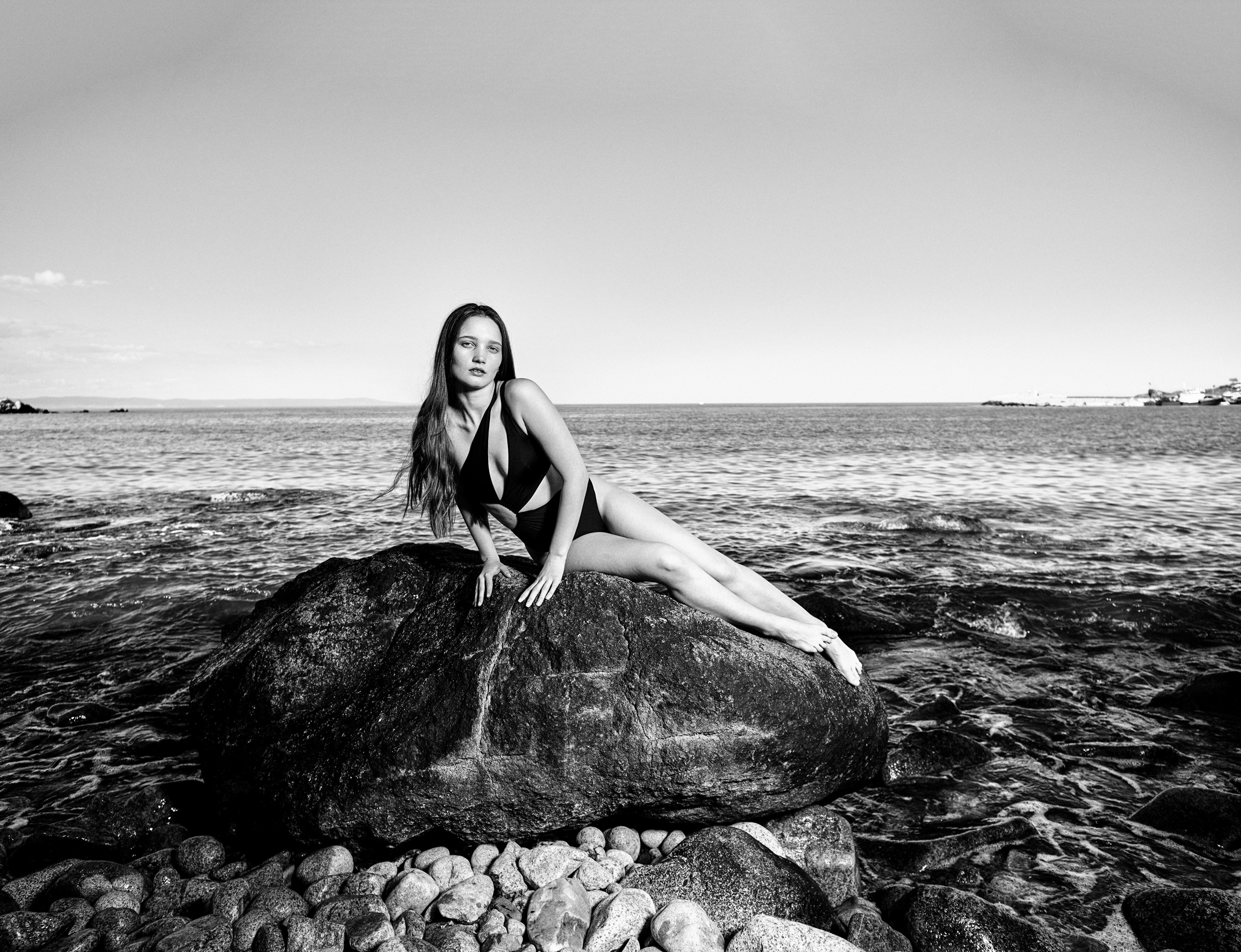 Woman in black swimsuit posing on rocky Black Sea coast